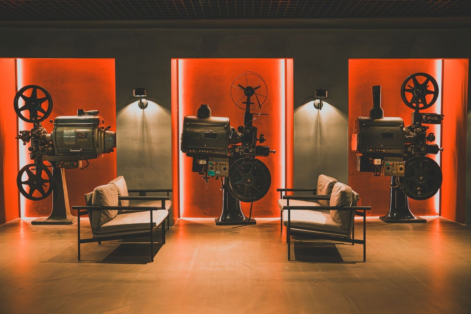 Three vintage film projectors displayed under dramatic red lighting